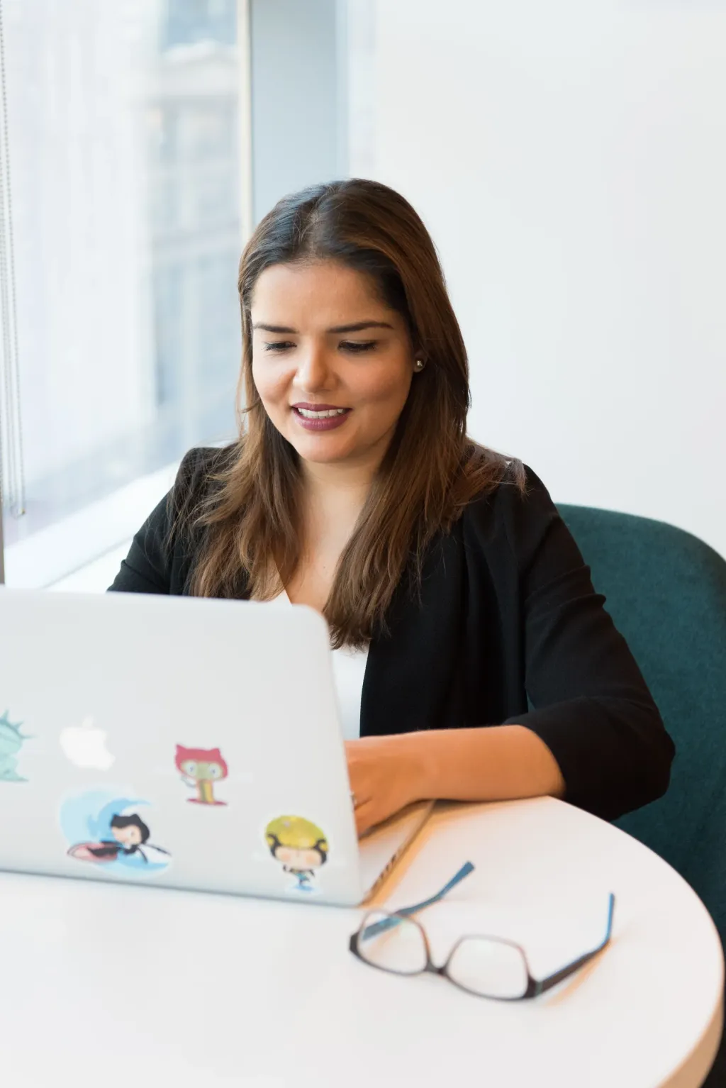 Photo: Christina Morillo. Source: Pexels. Stock photography. A smiling woman working on her laptop beside a window